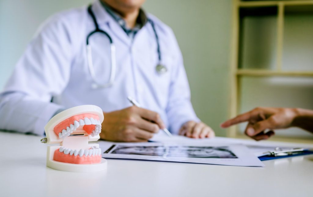 Gebissmodell am Tisch, im Hintergrund Zahnarzt, der auf Röntgenbild tippt und eine Hand eines anderen Menschen, Dr. Bruhn Zahnarztpraxis Berlin-Süd